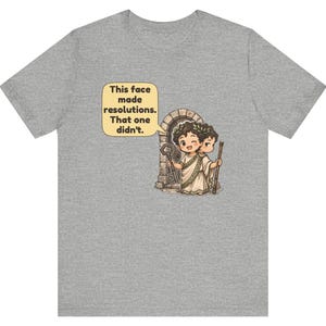 K&ouml;nnte beinhalten: Ein graues meliertes T-Shirt mit einer Grafik einer r&ouml;mischen Figur mit zwei Gesichtern, die einen Lorbeerkranz tr&auml;gt und einen Schl&uuml;ssel sowie einen Stab vor einem Torbogen h&auml;lt. Eine Sprechblase enth&auml;lt den Text: This face made resolutions. That one didn't.