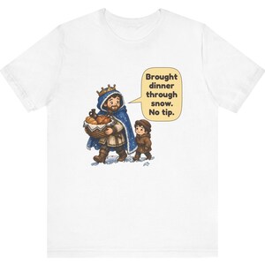 May include: A white short-sleeve t-shirt featuring a graphic of a king in a blue cloak carrying a basket of bread and a child walking through snow. A speech bubble contains the text: Brought dinner through snow. No tip.