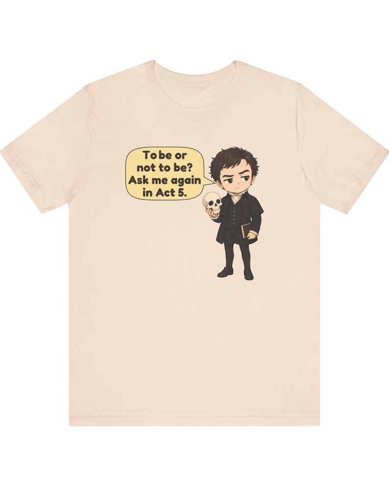 以下が含まれることがあります： 薄いベージュ色のTシャツ。黒い歴史的な衣装を着て頭蓋骨を持っているキャラクターの漫画風イラストが描かれています。黄色い吹き出しには「To be or not to be? Ask me again in Act 5.」というテキストが含まれています。