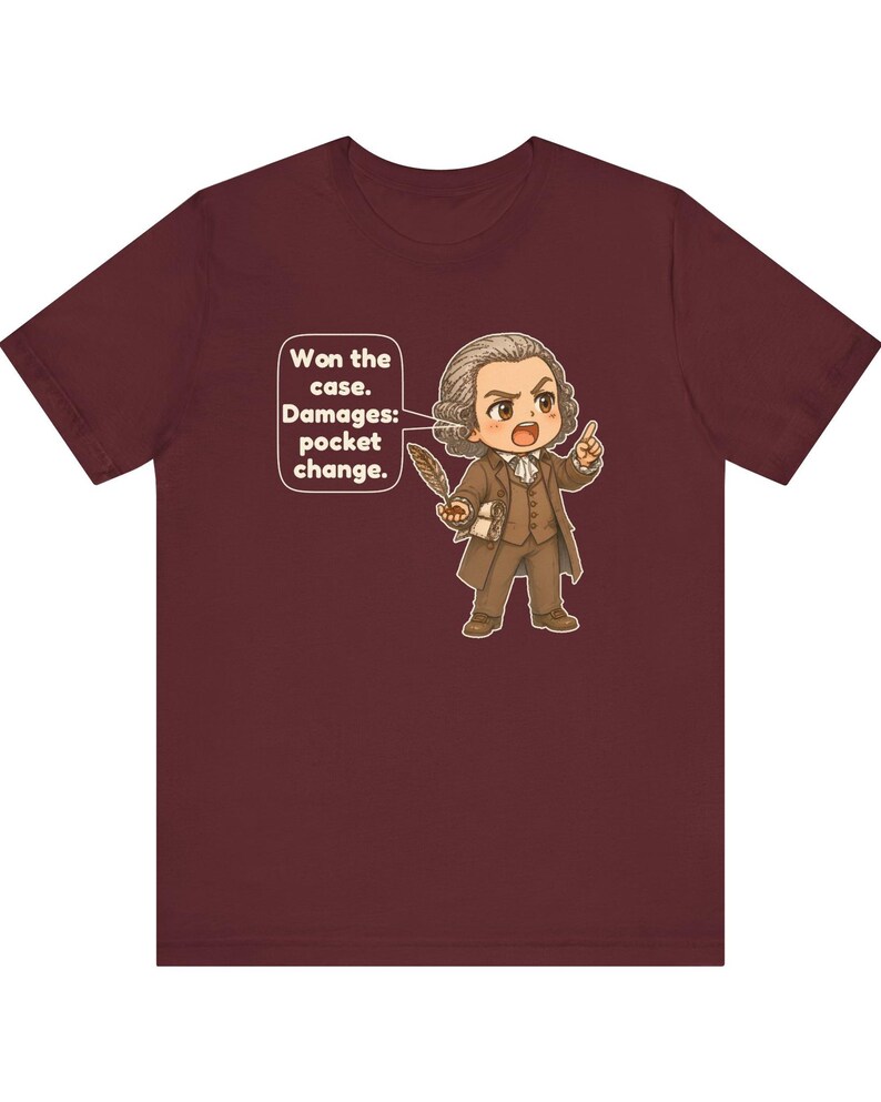 May include: A maroon short-sleeve t-shirt featuring a cartoon illustration of a lawyer in 18th-century attire holding a quill. A speech bubble contains the text: Won the case. Damages: pocket change.