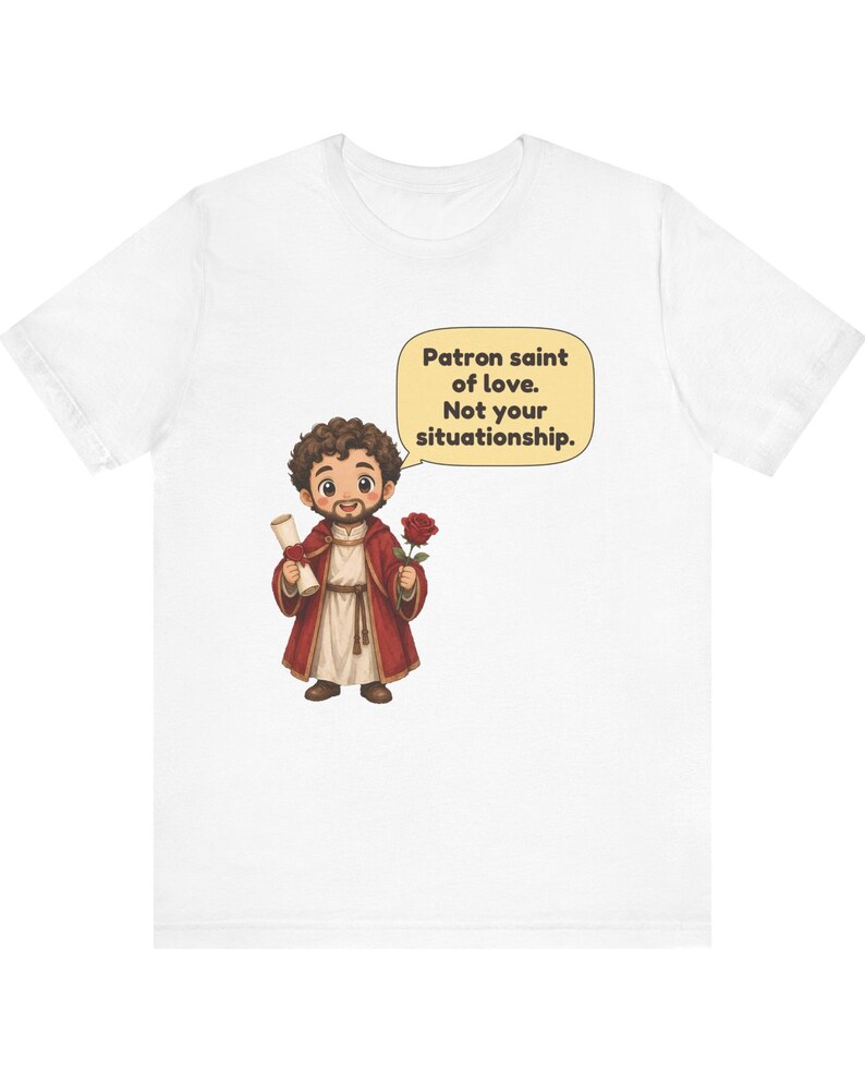 Puede incluir: Una camiseta blanca con una ilustraci&oacute;n de dibujos animados de una figura barbuda con t&uacute;nica roja que sostiene un pergamino y una rosa roja. Un globo de texto junto a la figura contiene el texto: Patron saint of love. Not your situationship.