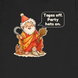 May include: A black t-shirt featuring a cartoon illustration of a bearded figure wearing a red party hat, a yellow and red toga, and white leg wraps. The figure holds a sickle and wheat, with a speech bubble that reads: Togas off. Party hats on.