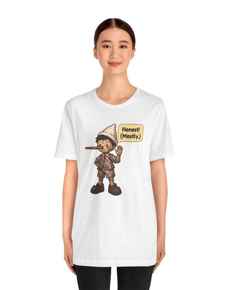 K&ouml;nnte beinhalten: Ein wei&szlig;es Kurzarm-T-Shirt mit einer Grafik einer Holzpuppe mit langer Nase, die einen Hut und eine kurze Hose tr&auml;gt. Die Figur winkt mit einer Hand und eine Sprechblase neben ihr enth&auml;lt den Text: Honest! (Mostly.)