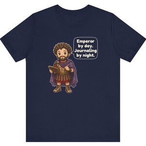 K&ouml;nnte beinhalten: Ein marineblaues T-Shirt mit einer Cartoon-Illustration eines b&auml;rtigen Kaisers in r&ouml;mischer R&uuml;stung und violettem Umhang, der ein Tagebuch und einen Stift h&auml;lt. Eine Sprechblase enth&auml;lt den Text: Emperor by day. Journaling by night.