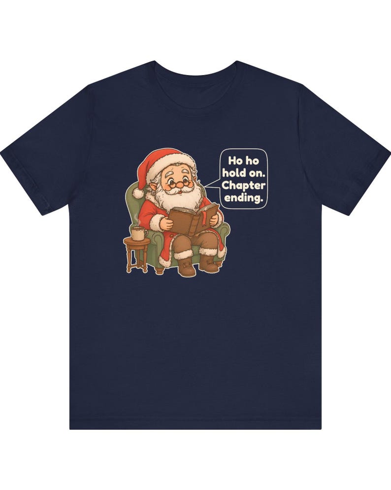 Op de afbeelding: Een marineblauw t-shirt met een afbeelding van de Kerstman die in een groene fauteuil zit, een boek leest en een mok op een bijzettafel heeft staan. Een tekstballon bevat de tekst: Ho ho hold on. Chapter ending.