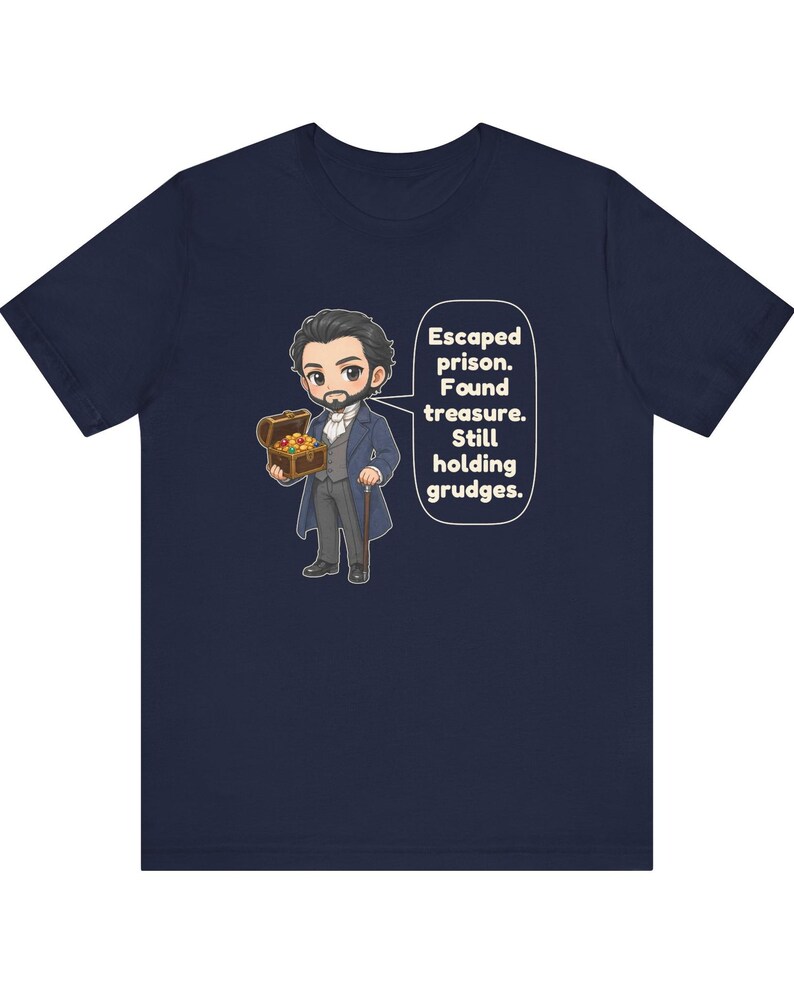 May include: A navy blue t-shirt featuring a cartoon illustration of a bearded man in a formal coat holding a treasure chest. A speech bubble next to him contains the text: Escaped prison. Found treasure. Still holding grudges.