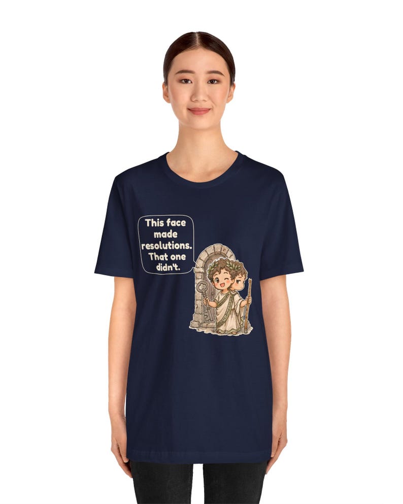 K&ouml;nnte beinhalten: Ein marineblaues T-Shirt mit einer Grafik einer r&ouml;mischen Figur mit zwei Gesichtern vor einem Torbogen. Die Figur h&auml;lt einen Schl&uuml;ssel und einen Stab. Eine Sprechblase enth&auml;lt den Text: This face made resolutions. That one didn't.