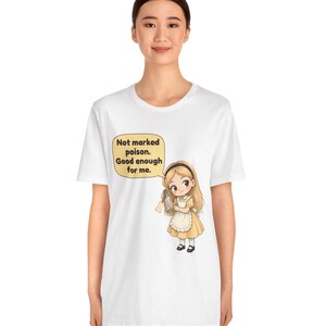 May include: A white short-sleeve t-shirt featuring a cartoon illustration of a girl with blonde hair wearing a yellow dress and white apron. She holds a small glass bottle. A speech bubble above her reads: Not marked poison. Good enough for me.