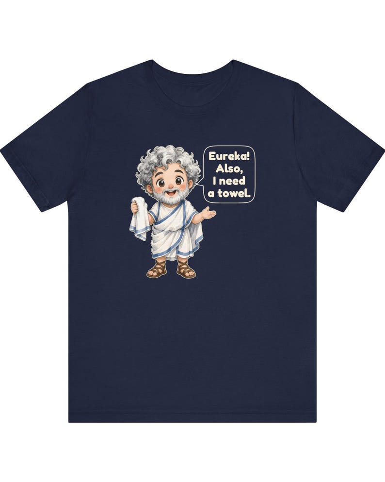 May include: A navy blue t-shirt featuring a cartoon illustration of a bearded figure with curly gray hair wearing a white toga and brown sandals. The figure holds a white towel and a speech bubble reads, Eureka! Also, I need a towel.
