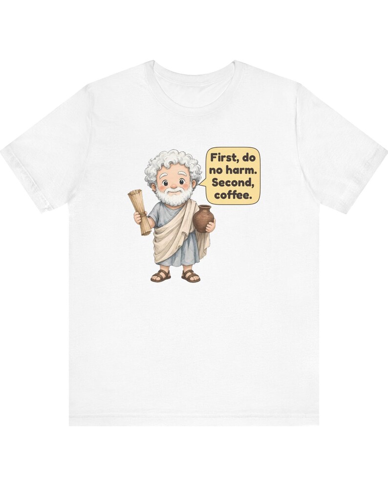 May include: A white t-shirt featuring a cartoon illustration of a bearded man in a toga holding a scroll and a brown pot. A yellow speech bubble next to the figure contains the black text: First, do no harm. Second, coffee.