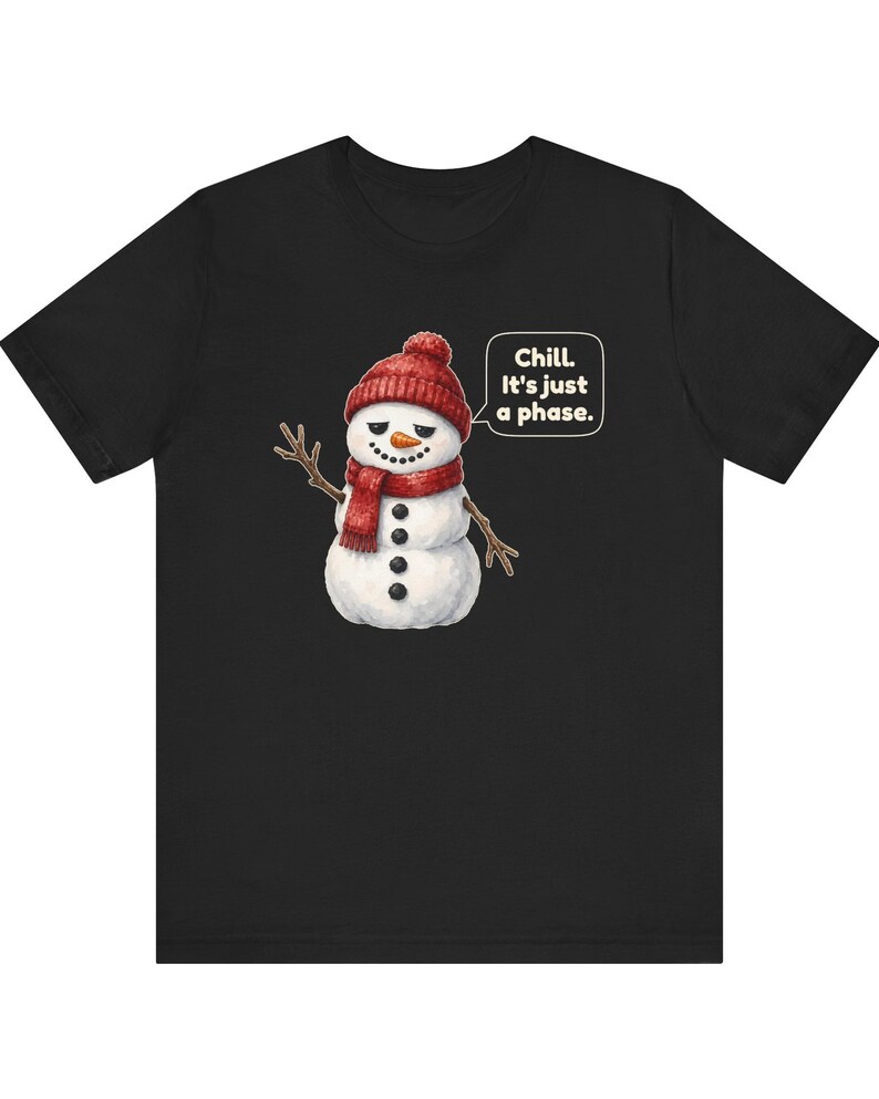 Pode incluir: Uma t-shirt preta de manga curta com o gr&aacute;fico de um boneco de neve a usar um gorro e um cachecol de malha vermelhos. O boneco de neve tem bra&ccedil;os de ramo, um nariz de cenoura e um bal&atilde;o com o texto branco: Chill. It's just a phase.