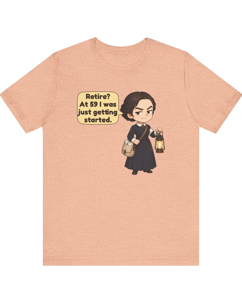 May include: A peach-colored t-shirt featuring a cartoon illustration of a person in a dark dress carrying a satchel and a lit lantern. A speech bubble next to the character contains the text: Retire? At 59 I was just getting started.