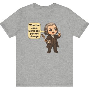 May include: A heather gray t-shirt featuring a cartoon illustration of a lawyer in 18th-century attire holding a quill and a document. A speech bubble contains the text: Won the case. Damages: pocket change.