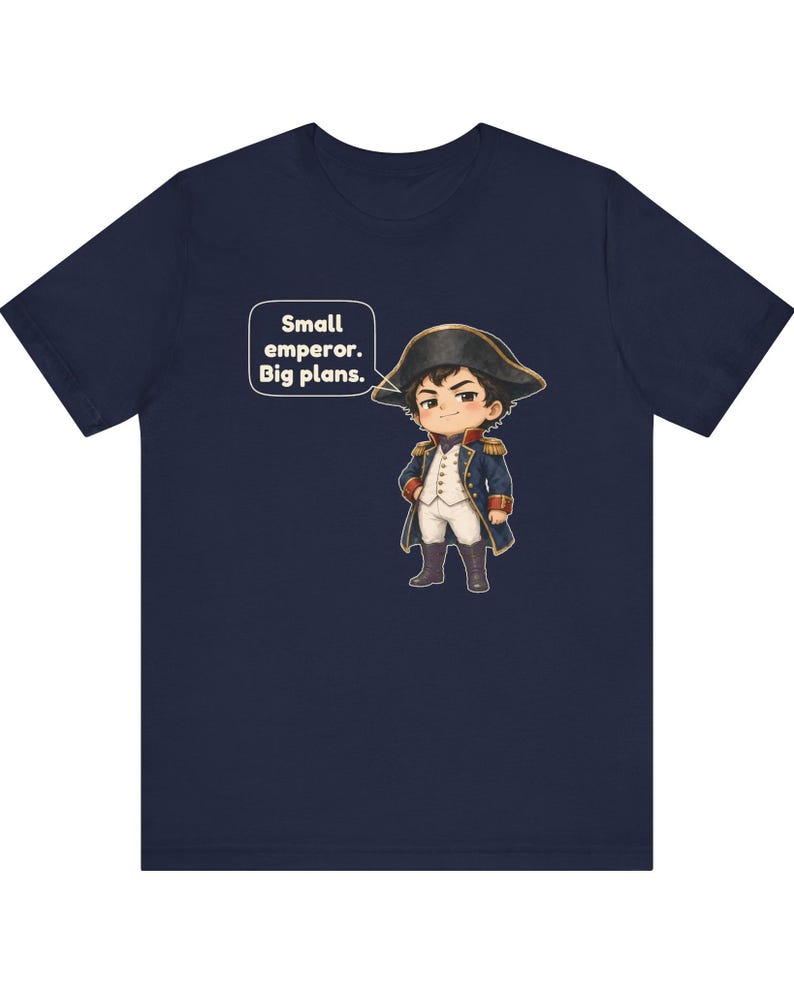 May include: A navy blue t-shirt featuring a cartoon illustration of a small figure dressed in a historical military uniform with a bicorne hat. A speech bubble next to the character contains the text: Small emperor. Big plans.