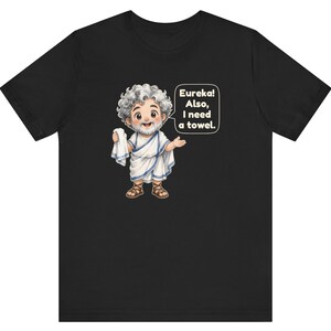 May include: A black t-shirt featuring a cartoon illustration of a bearded man with curly gray hair wearing a white toga and brown sandals. The character holds a white towel and has a speech bubble that reads, Eureka! Also, I need a towel.