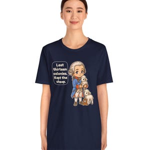 Peut inclure: Un t-shirt bleu marine &agrave; manches courtes avec une illustration de style dessin anim&eacute; repr&eacute;sentant un personnage historique en manteau bleu tenant un agneau blanc, avec un autre agneau &agrave; c&ocirc;t&eacute;. Une bulle contient le texte : Lost thirteen colonies. Kept the sheep.