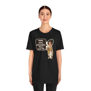 May include: A black short-sleeve t-shirt featuring a cartoon illustration of a person in ancient-style clothing holding an astrolabe. A speech bubble contains the text: Math, stars, philosophy. Pick a lane? No.