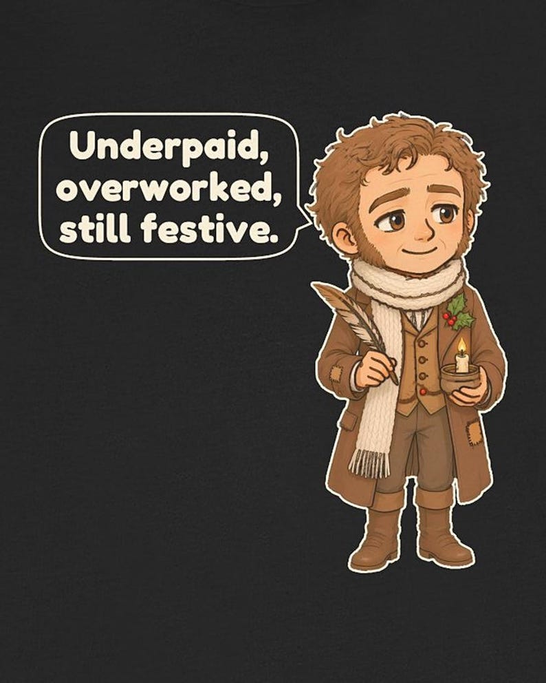 May include: A black t-shirt featuring a cartoon illustration of a person in brown Victorian-style clothing, a white scarf, and boots. The person holds a quill and a candle with holly. A speech bubble contains the text: Underpaid, overworked, still festive.