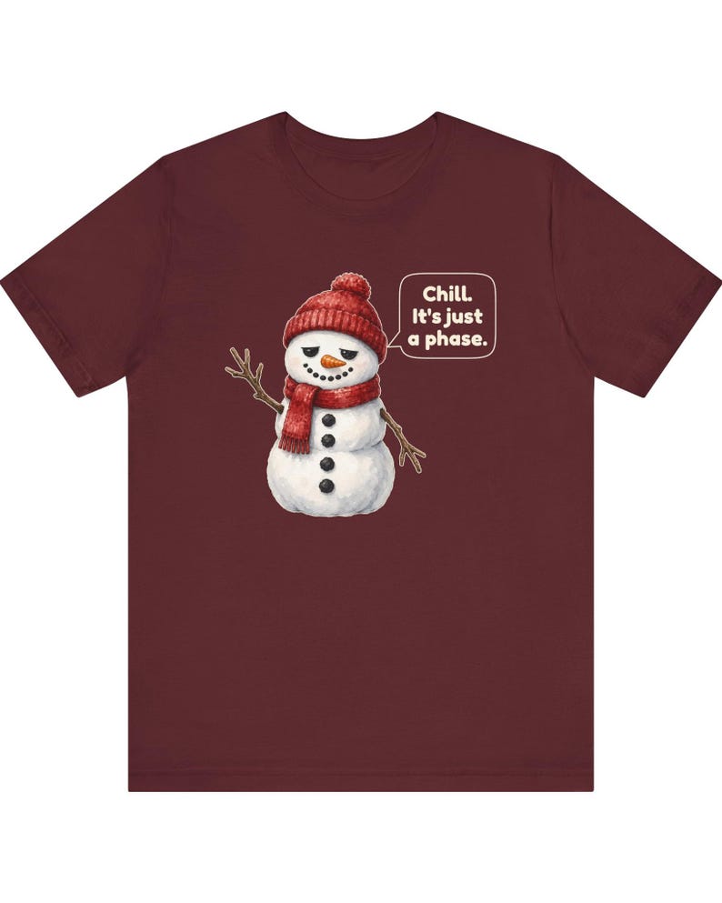 Pode incluir: Uma t-shirt de manga curta cor de vinho com o gr&aacute;fico de um boneco de neve a usar um gorro e um cachecol de malha vermelhos. O boneco de neve tem um nariz de cenoura, bra&ccedil;os de pau e um bal&atilde;o com o texto, Chill. It's just a phase.