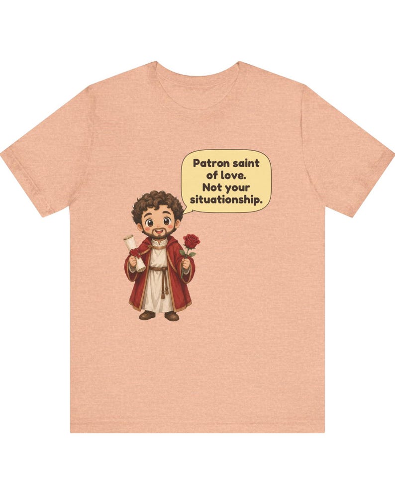 Puede incluir: Una camiseta color melocot&oacute;n con una ilustraci&oacute;n de dibujos animados de una figura barbuda con t&uacute;nica roja que sostiene un pergamino y una rosa roja. Un bocadillo sobre la figura contiene el texto: Patron saint of love. Not your situationship.