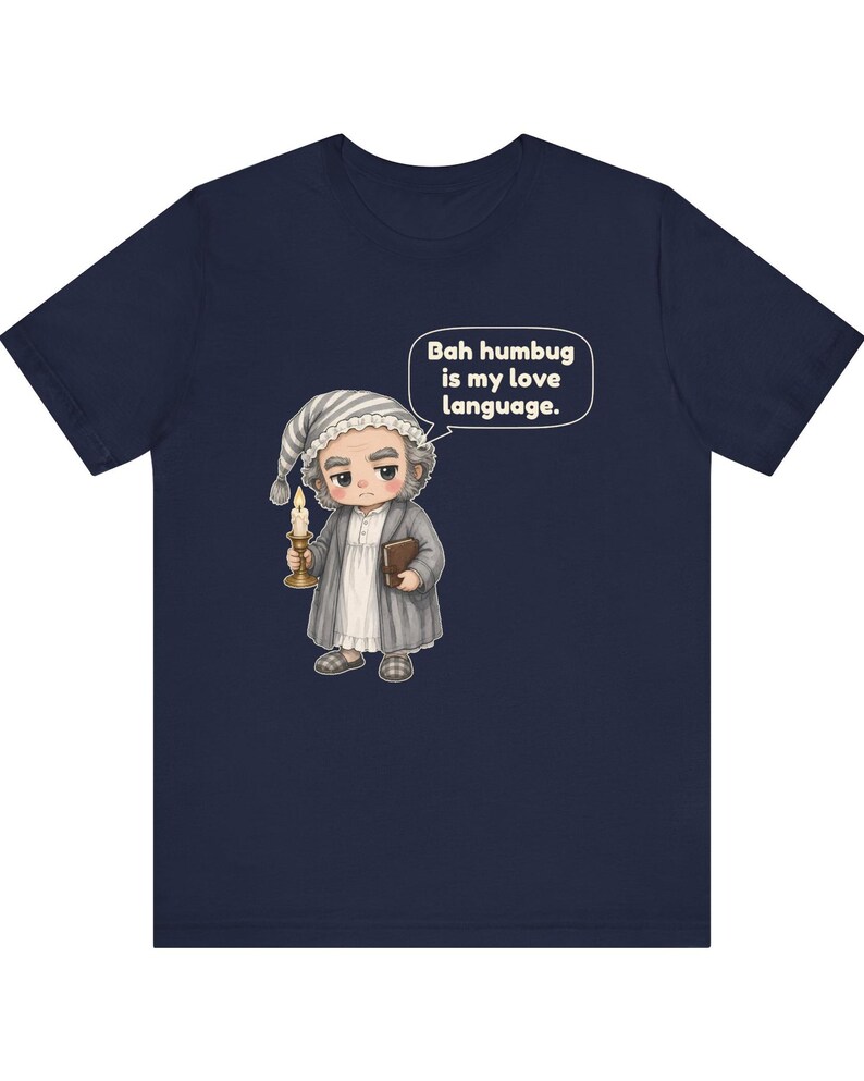 Puede incluir: Una camiseta azul marino de manga corta con una ilustraci&oacute;n de dibujos animados de un personaje con gorro de dormir y bata que sostiene una vela y un libro. Un globo de texto sobre el personaje contiene el texto, Bah humbug is my love language.