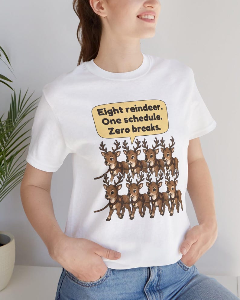 K&ouml;nnte beinhalten: Ein wei&szlig;es Kurzarm-T-Shirt mit einer Grafik von acht braunen Rentieren, die in zwei Reihen angeordnet sind. &Uuml;ber den Rentieren befindet sich eine gelbe Sprechblase mit dem schwarzen Text: Eight reindeer. One schedule. Zero breaks.