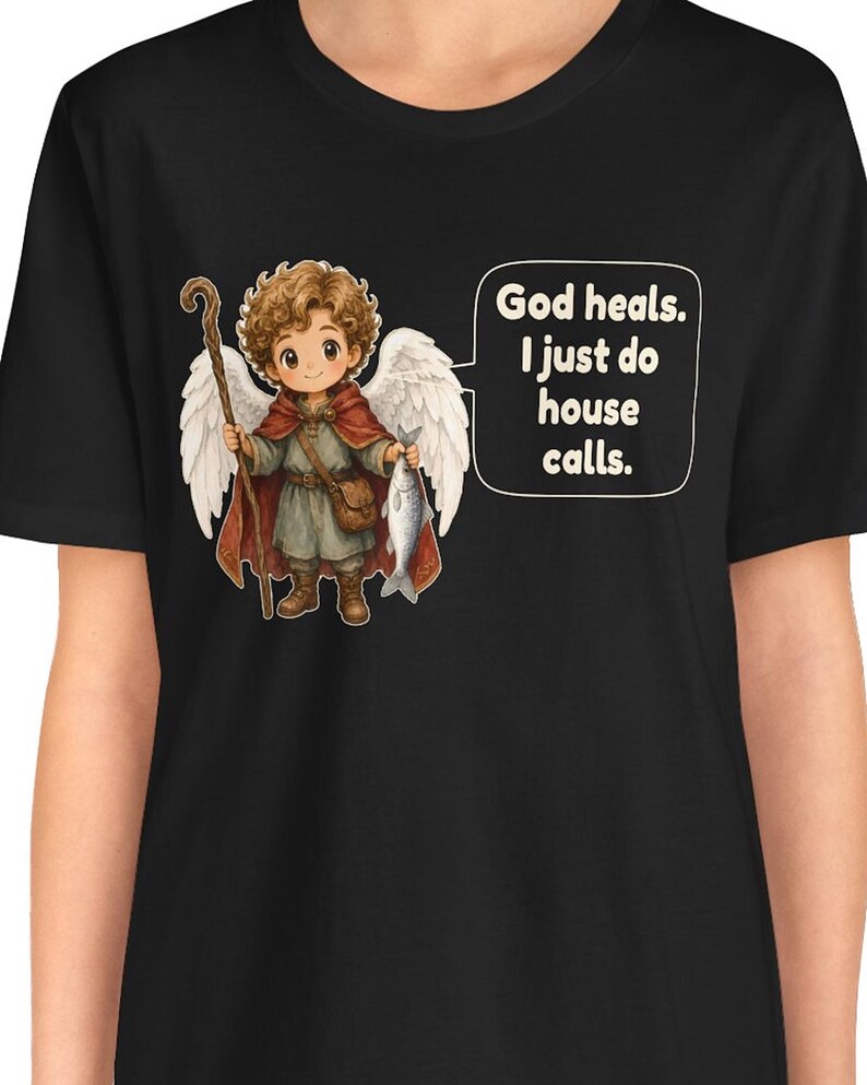 May include: A black t-shirt featuring a graphic of a curly-haired angel with white wings, wearing a red cloak and brown tunic, holding a wooden staff and a fish. A speech bubble next to the angel contains the text: God heals. I just do house calls.