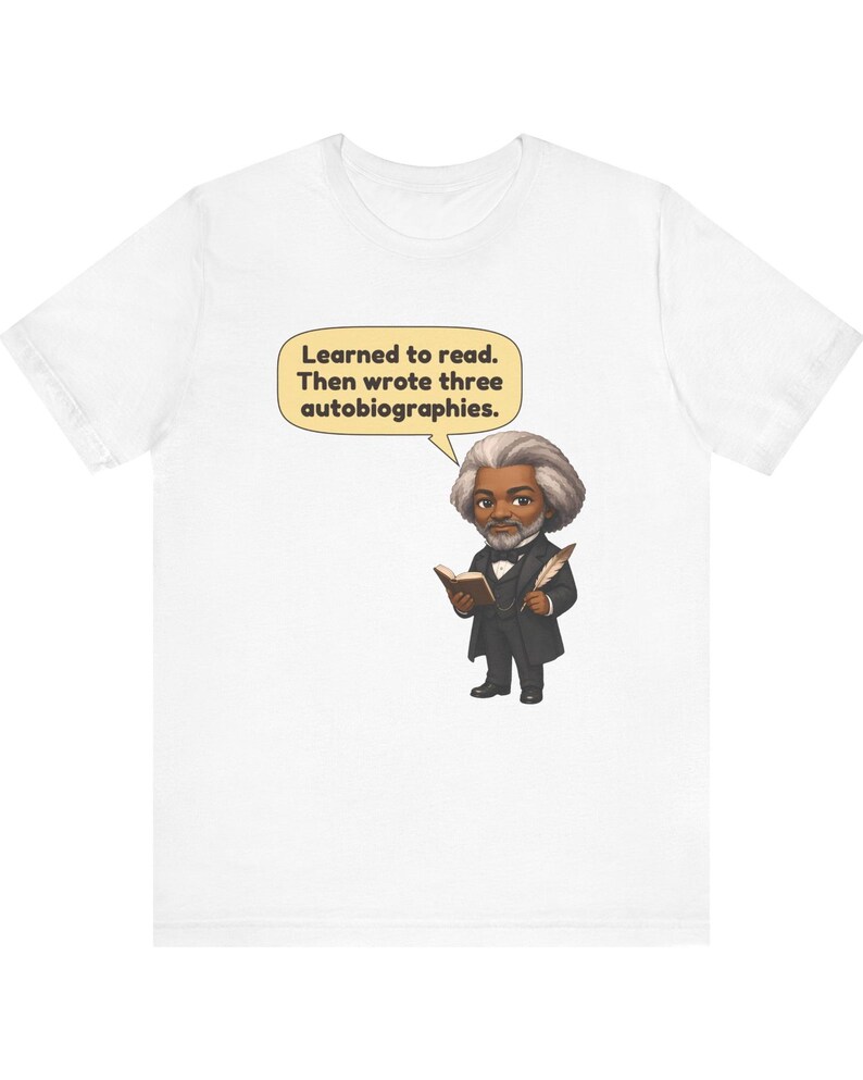 Puede incluir: Una camiseta blanca con una ilustraci&oacute;n de dibujos animados de Frederick Douglass sosteniendo un libro y una pluma. Un globo de texto sobre la figura contiene el texto: Learned to read. Then wrote three autobiographies.