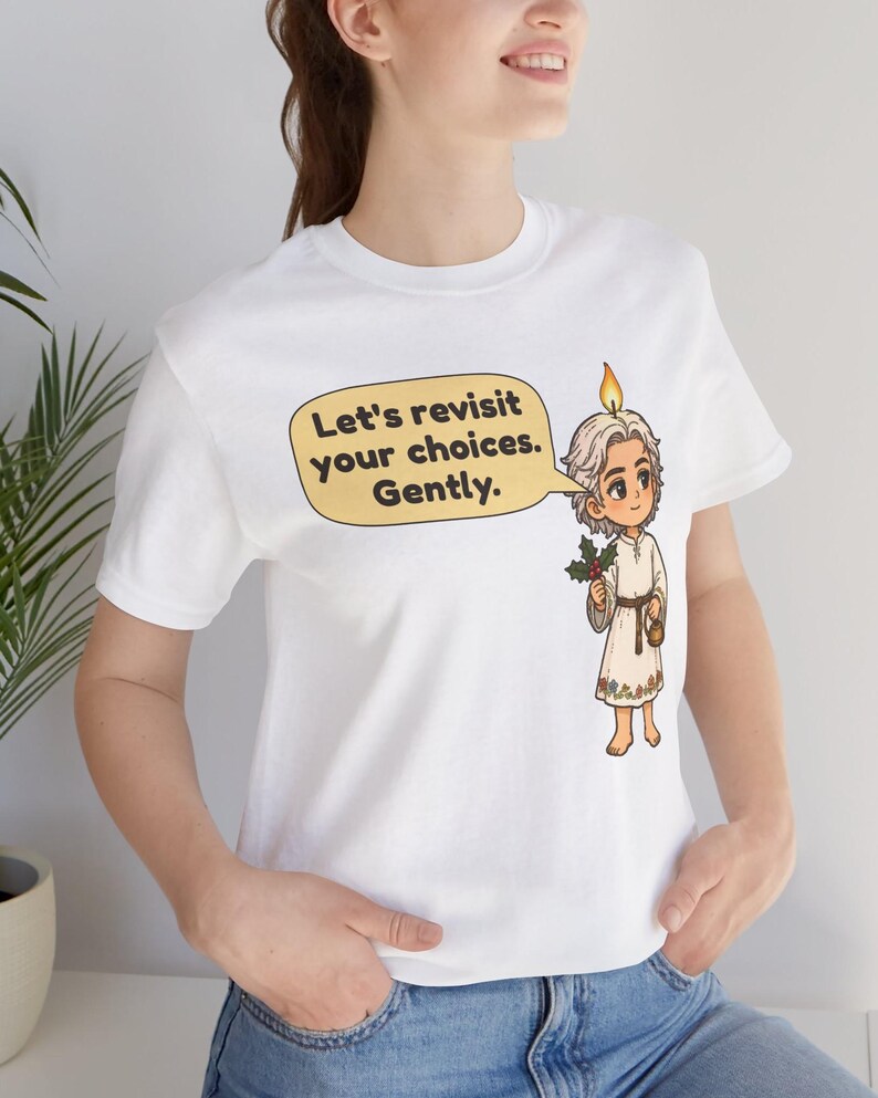 May include: A white short-sleeved t-shirt featuring a cartoon illustration of a character with a candle flame on their head, holding a sprig of holly. A yellow speech bubble contains the text: Let's revisit your choices. Gently.