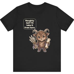 Puede incluir: Una camiseta negra con el gr&aacute;fico de una criatura marr&oacute;n, peluda y con cuernos que sostiene un manojo de palos y un pergamino. Un globo de texto sobre la criatura contiene el texto: Naughty list? I'll take it from here.