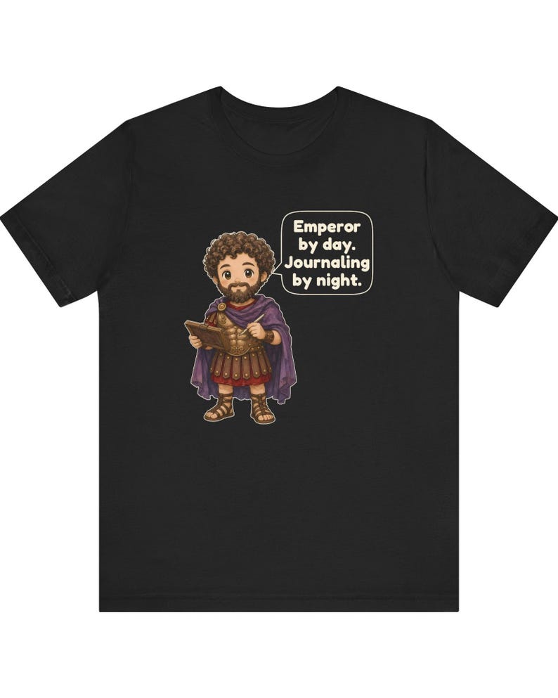 K&ouml;nnte beinhalten: Ein schwarzes T-Shirt mit einer Cartoon-Illustration eines b&auml;rtigen Kaisers in r&ouml;mischer R&uuml;stung und violettem Umhang, der ein Buch und einen Stift h&auml;lt. Eine Sprechblase enth&auml;lt den Text: Emperor by day. Journaling by night.