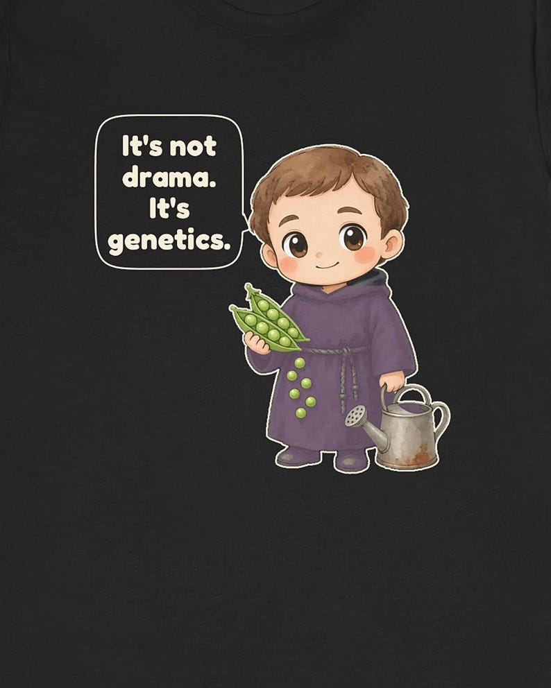 May include: A black t-shirt featuring a cartoon illustration of a monk in a purple robe holding a pea pod. The monk is next to a small watering can and a speech bubble with the text: It's not drama. It's genetics. Several green peas are scattered on the robe.