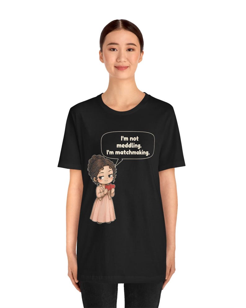 K&ouml;nnte beinhalten: Ein schwarzes T-Shirt mit kurzen &Auml;rmeln und einer Cartoon-Illustration einer Person mit braunen Haaren in einem hellrosa Kleid, die ein rotes Herz h&auml;lt. Eine Sprechblase enth&auml;lt den Text: I'm not meddling. I'm matchmaking.