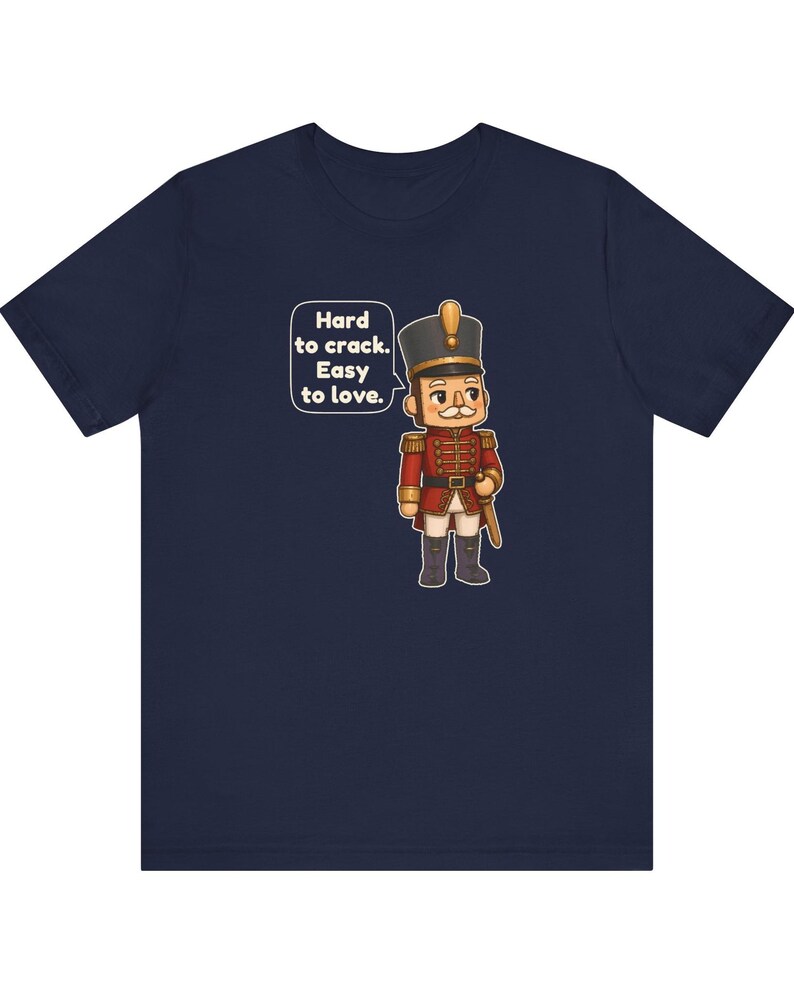 Pu&ograve; includere: Una t-shirt blu navy con la grafica di un soldatino schiaccianoci in uniforme rossa con dettagli dorati. Un fumetto accanto al personaggio riporta il testo: Hard to crack. Easy to love. Il disegno &egrave; centrato sulla parte anteriore.