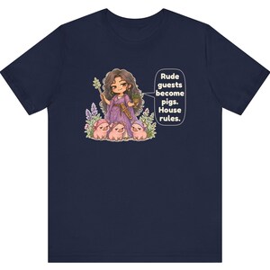 May include: A navy blue t-shirt featuring a graphic of a character in a purple dress holding a staff and a cup, surrounded by three small pigs. A speech bubble contains the text: Rude guests become pigs. House rules.