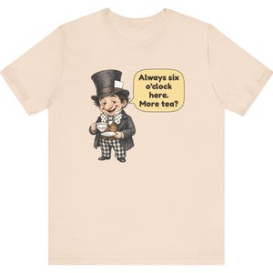 May include: A light beige t-shirt featuring a graphic of a character wearing a top hat, a brown vest, and a polka-dot bow tie, holding a teacup. A yellow speech bubble contains the text: Always six o'clock here. More tea?