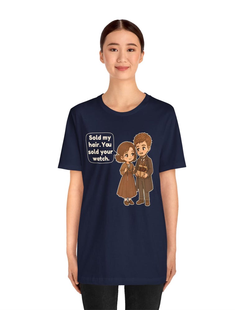 May include: A navy blue short-sleeve t-shirt featuring a cartoon illustration of two figures in brown clothing. A speech bubble contains the text: Sold my hair. You sold your watch. The design is centered on the front of the garment.