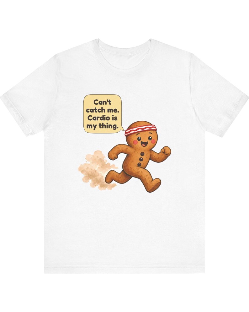 May include: A white t-shirt featuring a cartoon gingerbread person wearing a red and white striped headband, running and leaving a dust cloud behind. A speech bubble above contains the text: Can't catch me. Cardio is my thing.
