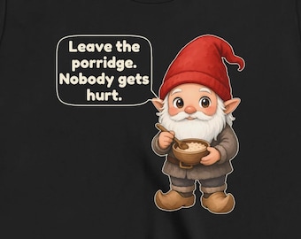 Pode incluir: Uma t-shirt preta com um gráfico de um gnomo com um chapéu vermelho e roupa castanha, segurando uma tigela e uma colher de madeira. Um balão de fala ao lado do gnomo contém o texto: Leave the porridge. Nobody gets hurt.