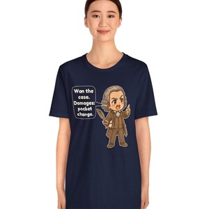 May include: A navy blue t-shirt featuring a cartoon illustration of a historical figure in a brown suit holding a quill. A speech bubble contains the text: Won the case. Damages: pocket change. The design is centered on the front of the shirt.