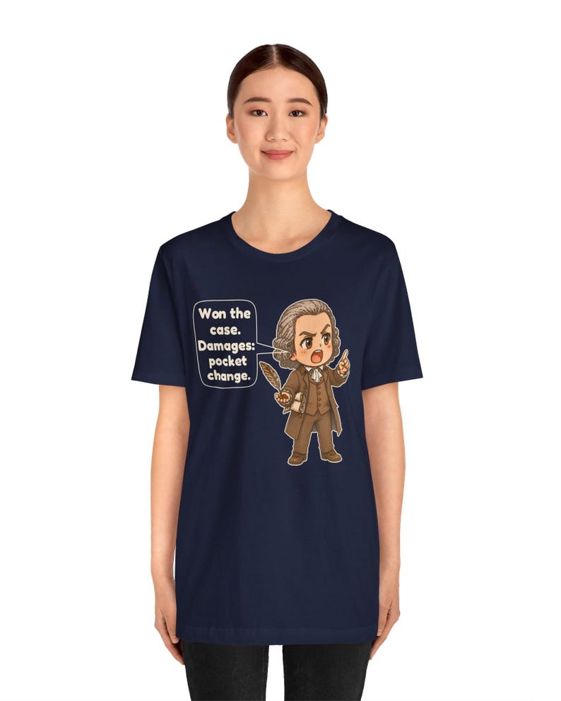 May include: A navy blue t-shirt featuring a cartoon illustration of a historical figure in a brown suit holding a quill. A speech bubble contains the text: Won the case. Damages: pocket change. The design is centered on the front of the shirt.