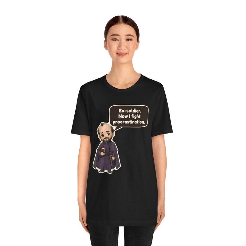 May include: A black short-sleeved t-shirt featuring a cartoon illustration of a bearded figure in a purple robe holding a book and sword. A speech bubble above the figure contains the text: Ex-soldier. Now I fight procrastination.