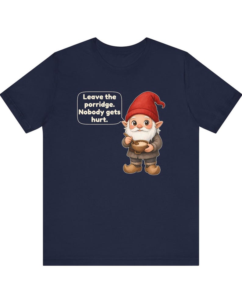 May include: A navy blue short-sleeve t-shirt featuring a graphic of a gnome wearing a red hat and brown clothing, holding a bowl of porridge with a spoon. A speech bubble next to the gnome contains the text: Leave the porridge. Nobody gets hurt.