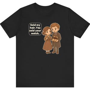 May include: A black t-shirt featuring a cartoon illustration of two people in brown clothing. One person holds a small box, and a speech bubble contains the text: Sold my hair. You sold your watch. The design is centered on the front of the shirt.