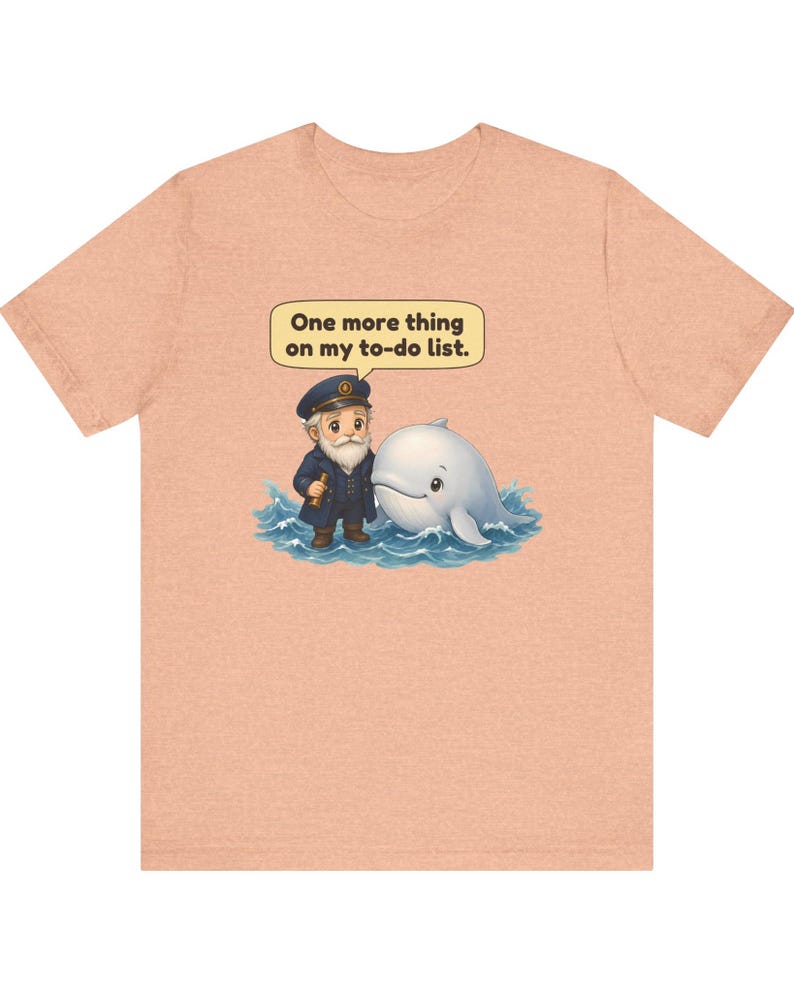May include: A peach-colored t-shirt featuring a graphic of a bearded captain in a navy uniform standing next to a white whale in blue water. Above them, a speech bubble contains the text: One more thing on my to-do list.