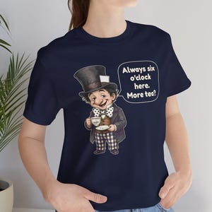 May include: A navy blue t-shirt featuring a graphic of a character in a top hat and bowtie holding a teacup. A speech bubble next to the character contains the text: Always six o'clock here. More tea? The character wears a dark jacket and checkered pants.