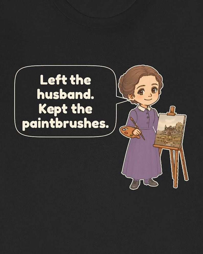May include: A black t-shirt featuring a cartoon illustration of a person in a purple dress holding a paint palette and brush next to an easel. A speech bubble contains the text: Left the husband. Kept the paintbrushes.