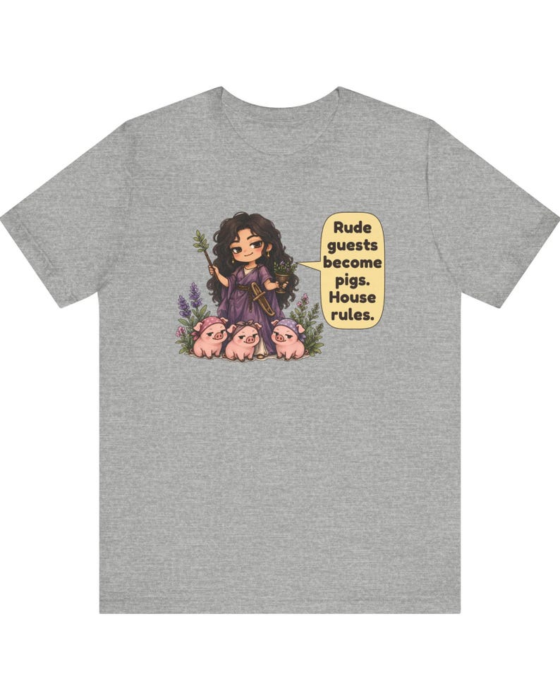 May include: A heather gray t-shirt featuring a cartoon illustration of a dark-haired figure in a purple robe holding a wand and goblet, surrounded by three small pigs. A speech bubble contains the text: Rude guests become pigs. House rules.