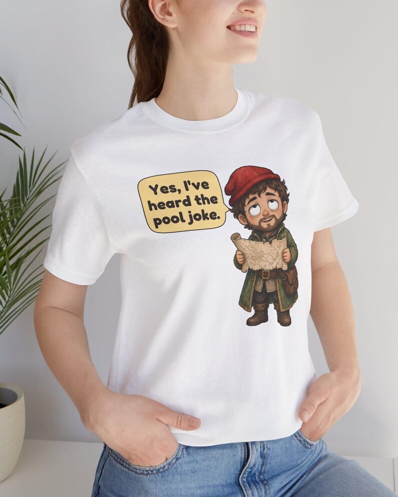 May include: A white t-shirt featuring a cartoon illustration of a bearded character wearing a red cap and green coat, holding a map. A yellow speech bubble next to the character contains the black text, Yes, I've heard the pool joke.
