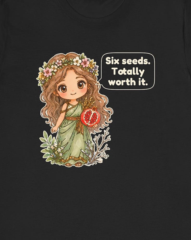 May include: A black t-shirt featuring a cartoon illustration of a character with long brown hair wearing a flower crown and a green dress. The character holds a pomegranate and a speech bubble reads: Six seeds. Totally worth it.
